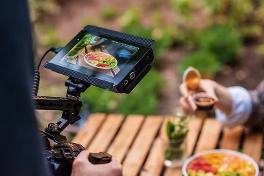 Camera-opstelling filmt een kom met voedsel op een houten tafel met een persoon die saus inschenkt op de achtergrond.